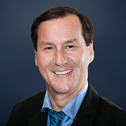 Brandt Worley smiles to the camera against a dark blue background.